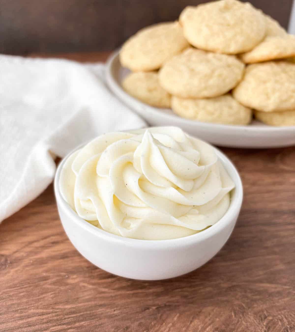 Small white bowl filled with Sour Cream Frosting with cookies in the background.