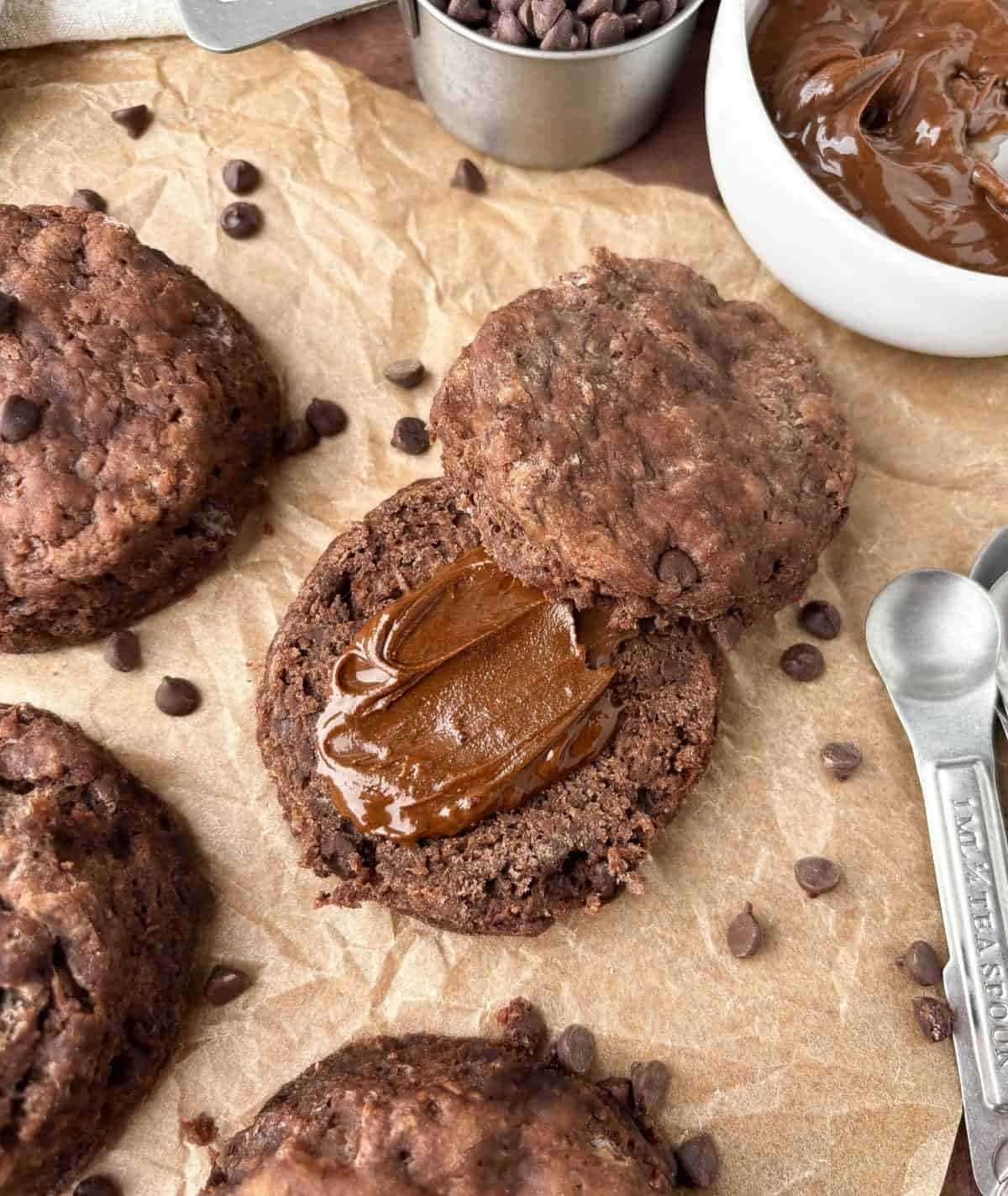 Top view of a split Chocolate Biscuit with chocolate hazelnut spread on parchment paper with more biscuits and chocolate chips.